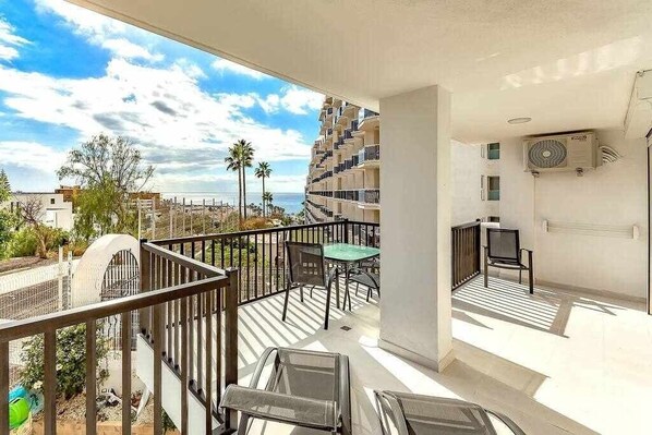 A balcony with a view of the sea, a table with chairs, and a TV. - Moderno apartamento en el Parque Royal I (Adeje)