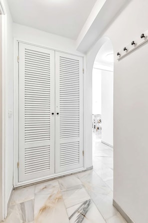 A hallway with a white door with horizontal slats, a marble floor, and a white wall with a light fixture. - Apartment in complex Altamira with direct sea view (Costa Adeje)