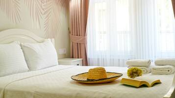 Un lit bien fait, avec du linge de lit blanc, un chapeau de paille, un livre et des serviettes, dans une chambre d’hôtel.