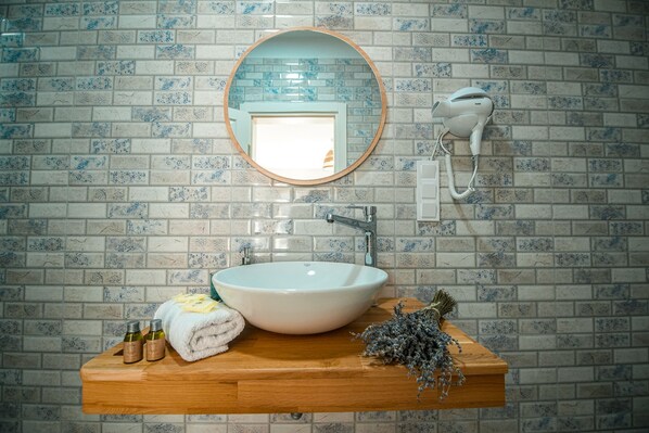A bathroom with a white sink, wooden vanity, a round mirror, and a hairdryer mounted on the wall. - Lutro Otel (Bozcaada)