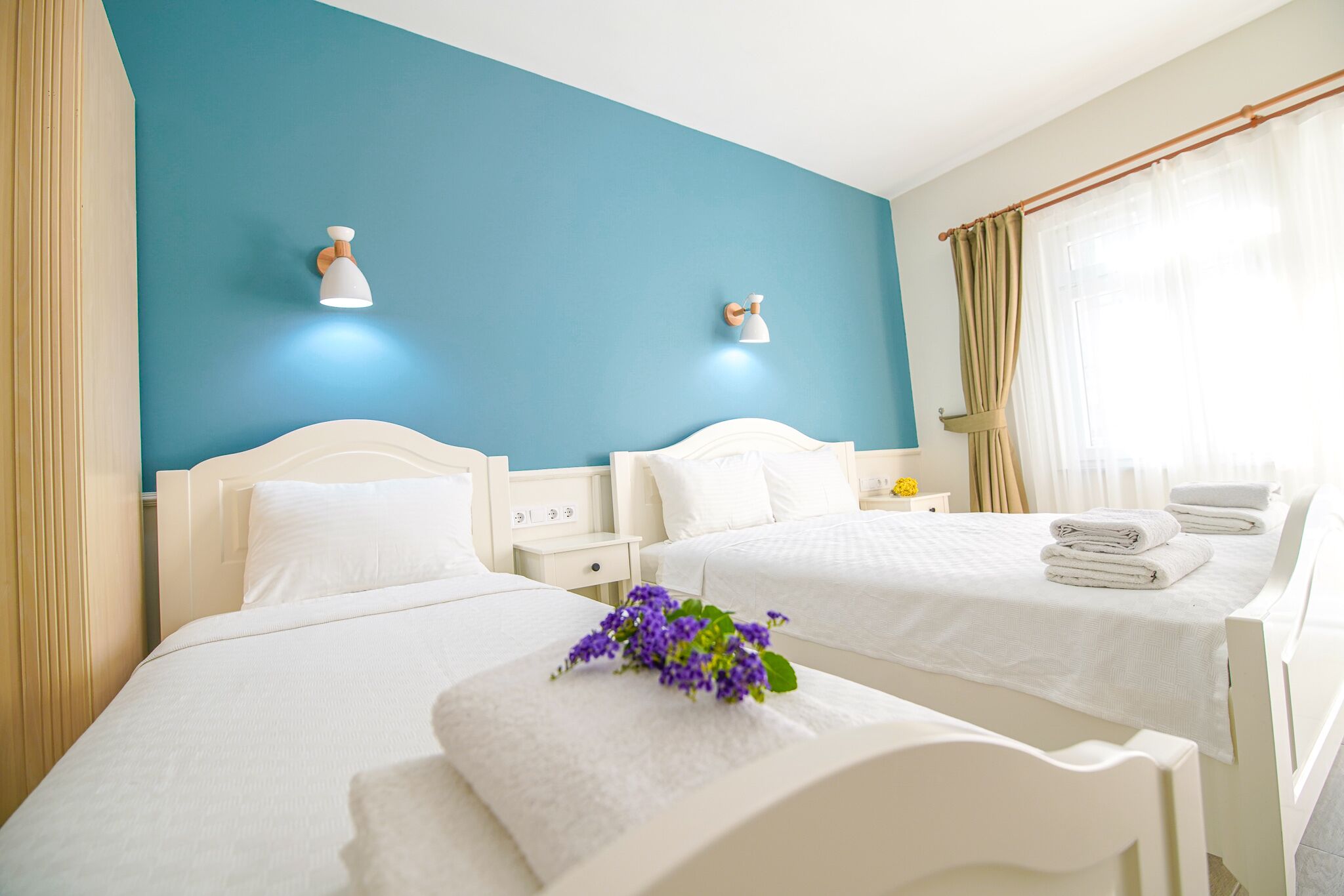 Habitación de hotel con dos camas, una pared azul de acento y una ventana con cortinas.