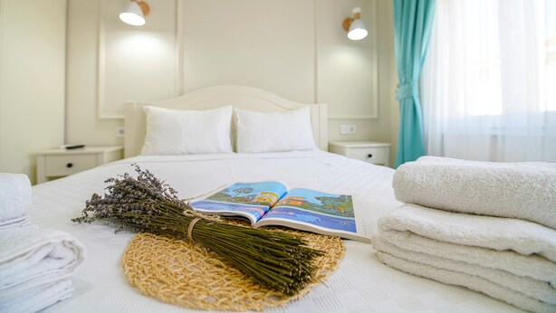 Uma cama bem arrumada com um livro, toalhas e um ramo de lavanda.