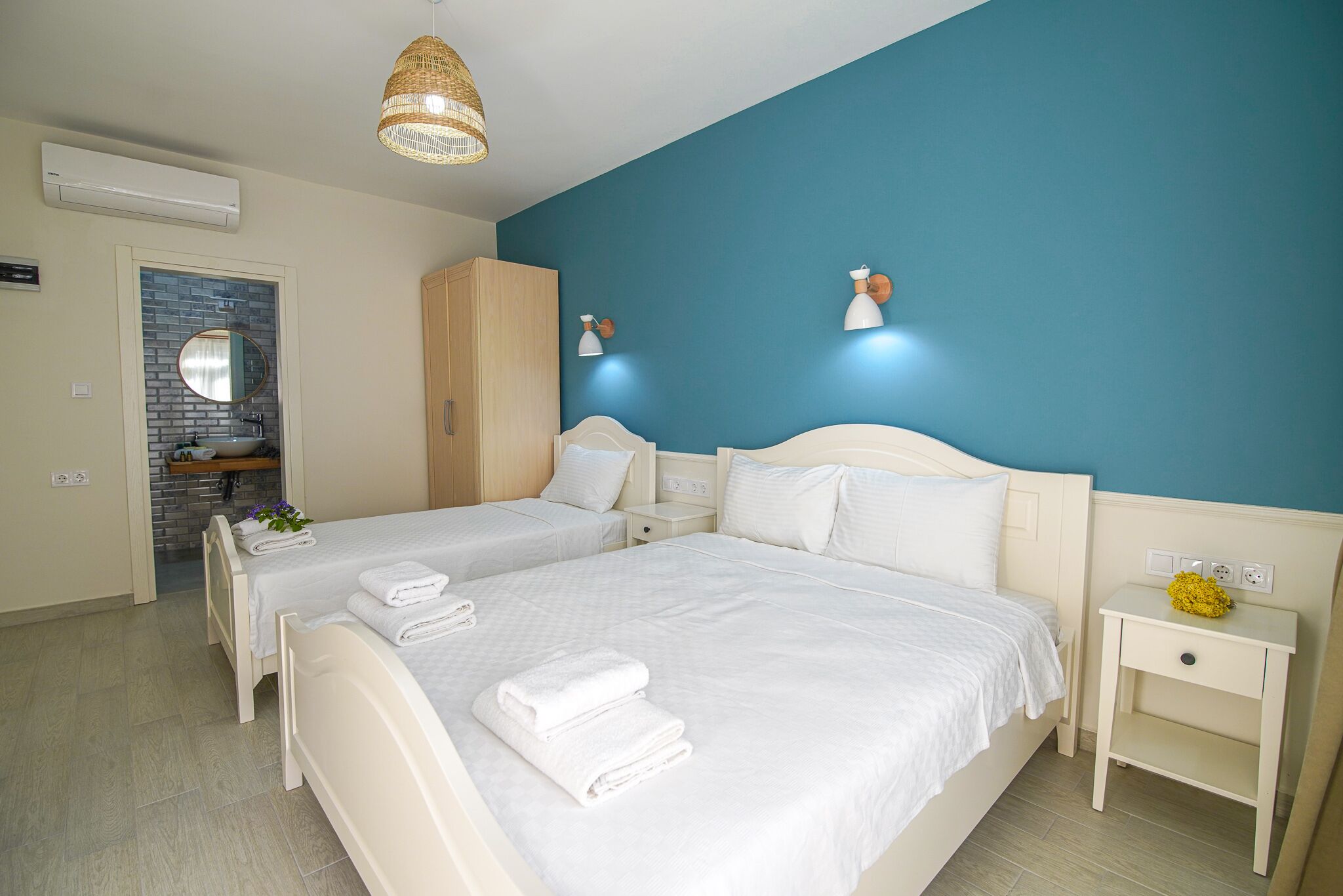 A hotel room with two beds, a bathroom with a mirror and sink, and a blue accent wall.