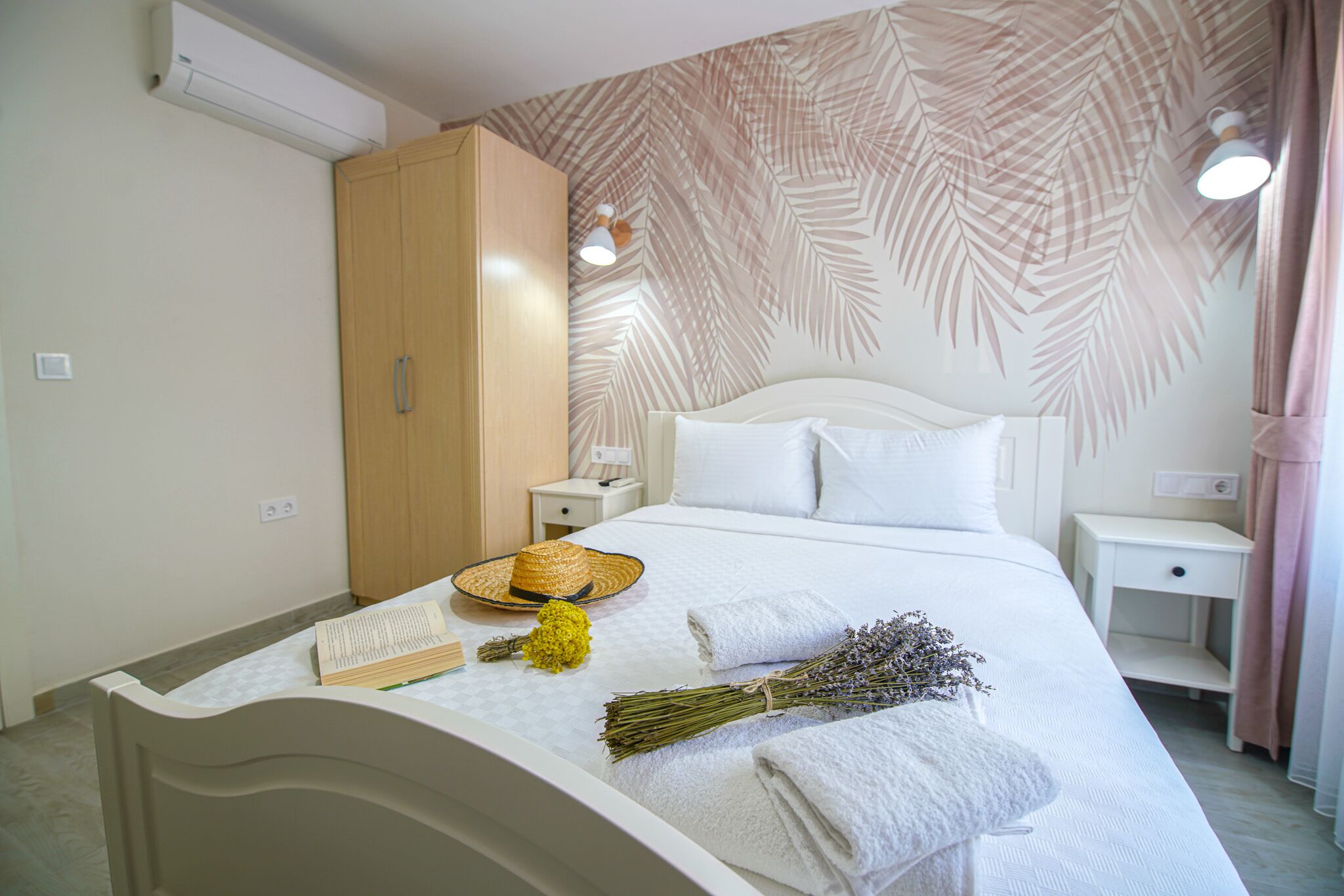 A neatly made bed with white linens, a bedside table with a lamp, a wardrobe, and a wall with a leaf pattern.