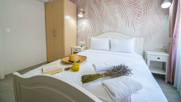 A neatly made bed with white linens, a bedside table with a lamp, a wardrobe, and a wall with a leaf pattern.