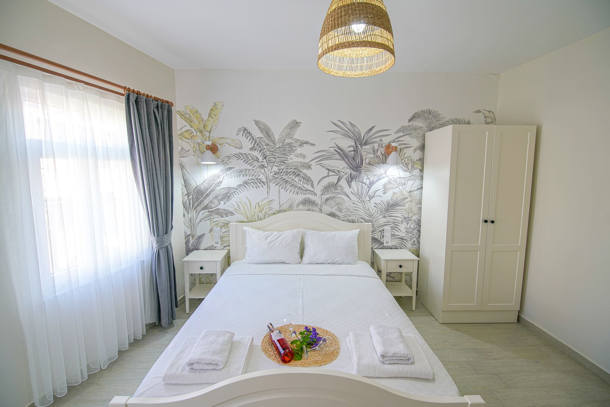 Une chambre à coucher bien aménagée, avec un lit, des tables de chevet, une armoire et une fresque murale sur le thème des pays tropicaux.