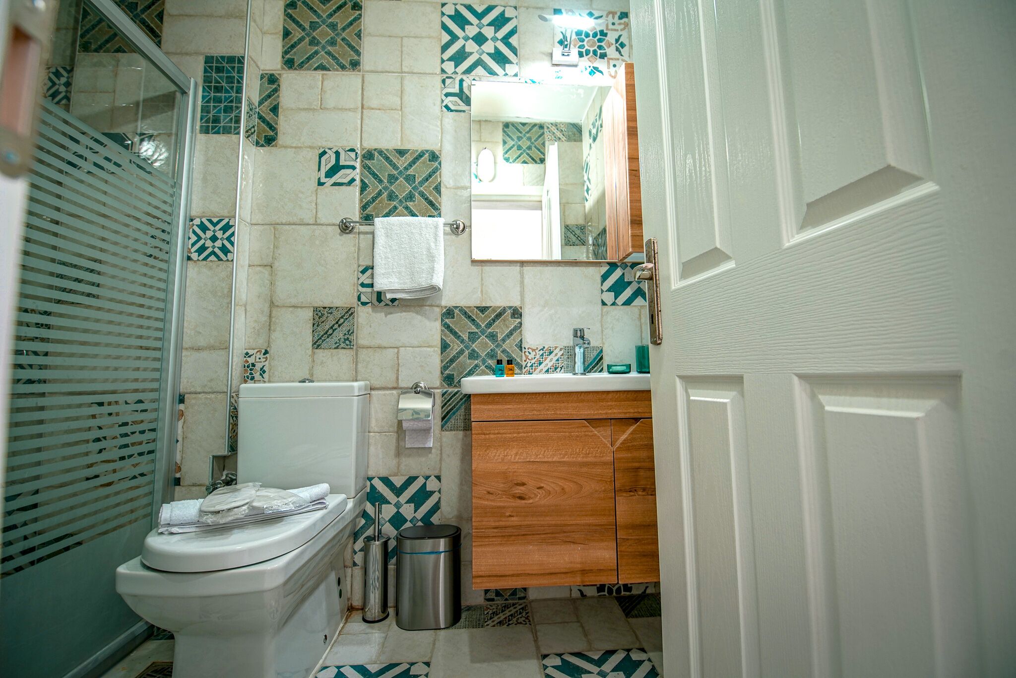 Un baño con inodoro, lavamanos, espejo y azulejos estampados.