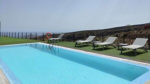 A swimming pool with white lounge chairs and a lifebuoy, surrounded by a grassy area and a rocky landscape. - Casa rural con vistas maravillosas en Arico (Santa Cruz de Tenerife)