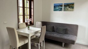 A dining area with a table and chairs, a window, a gray sofa, and two paintings on the wall. - Casa rural con vistas maravillosas en Arico (Santa Cruz de Tenerife)