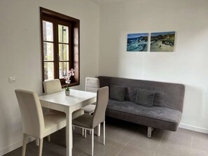 A dining area with a table and chairs, a window, a gray sofa, and two paintings on the wall.