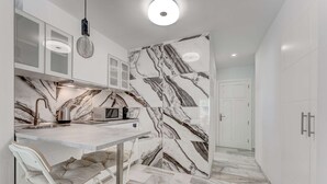 A modern kitchen with a marble backsplash, a built-in microwave, and a white dining area with a cushioned chair. - Graceful brand new studio in Altamira (Adeje)