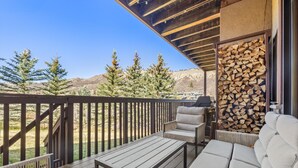 A wooden deck with a sofa and table, a grill, and a stack of firewood. - Snowmass Getaway Wraparound Decks & Valley Views - 229 #35 by RedAwning (Snowmass Village)