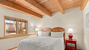 A bedroom with a wooden ceiling, a large bed with a grey bedspread, two bedside lamps, and a red nightstand. - Snowmass Getaway Wraparound Decks & Valley Views - 229 #35 by RedAwning (Snowmass Village)