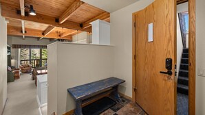 A hallway with a wooden door, a bench, and a view of a balcony area with outdoor furniture. - Snowmass Getaway Wraparound Decks & Valley Views - 229 #35 by RedAwning (Snowmass Village)