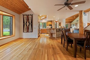 A spacious kitchen with wooden flooring, a dining area with a large table and chairs, and a view of the outdoors through large windows. - Glaze Meadow 376 3 Bedroom Home by RedAwning (Sisters)