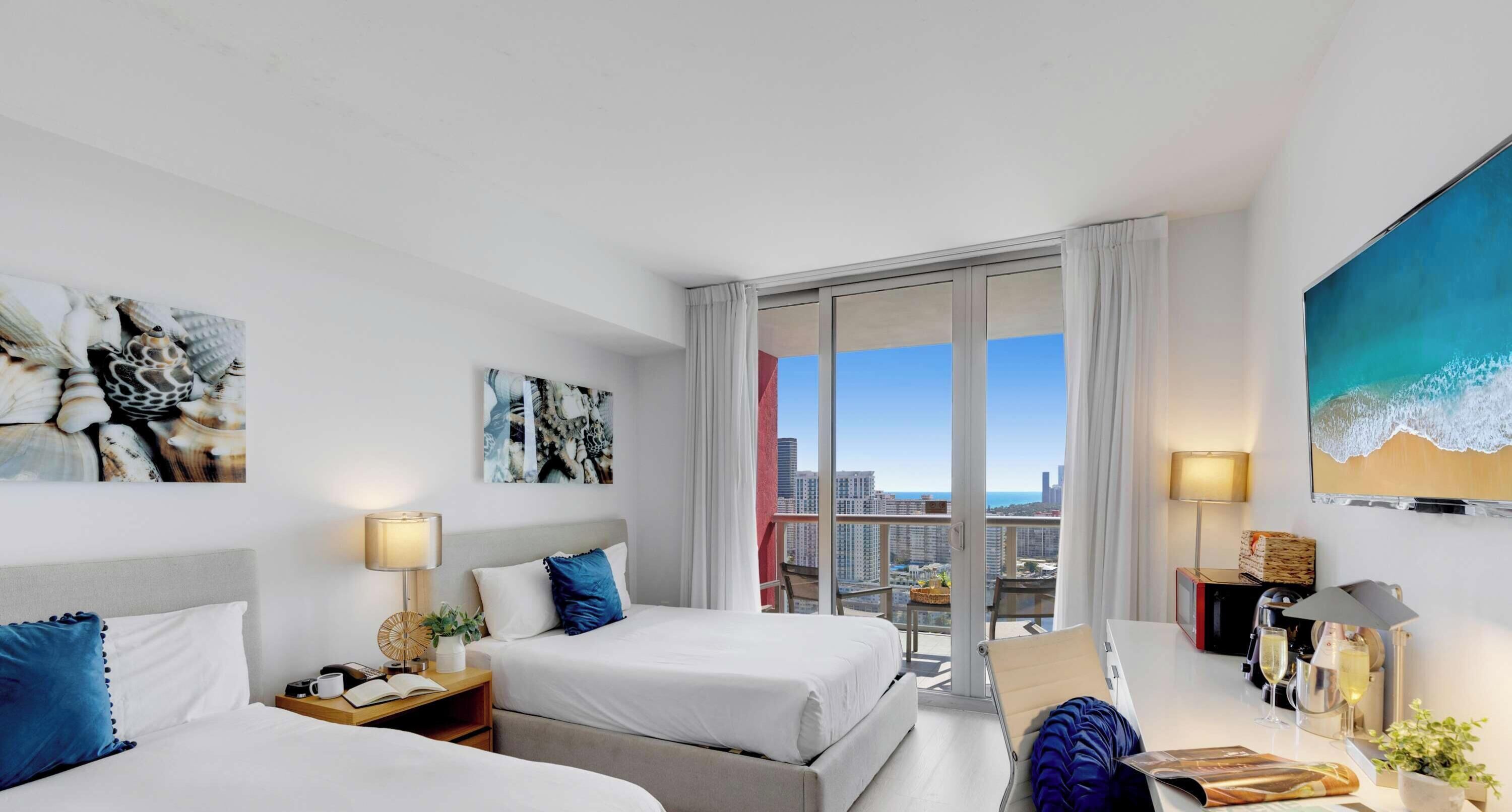 A hotel room with two beds, a balcony with a city view, and artwork on the walls.