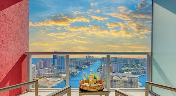 A balcony with a cityscape view, a table with a basket, and a bottle.