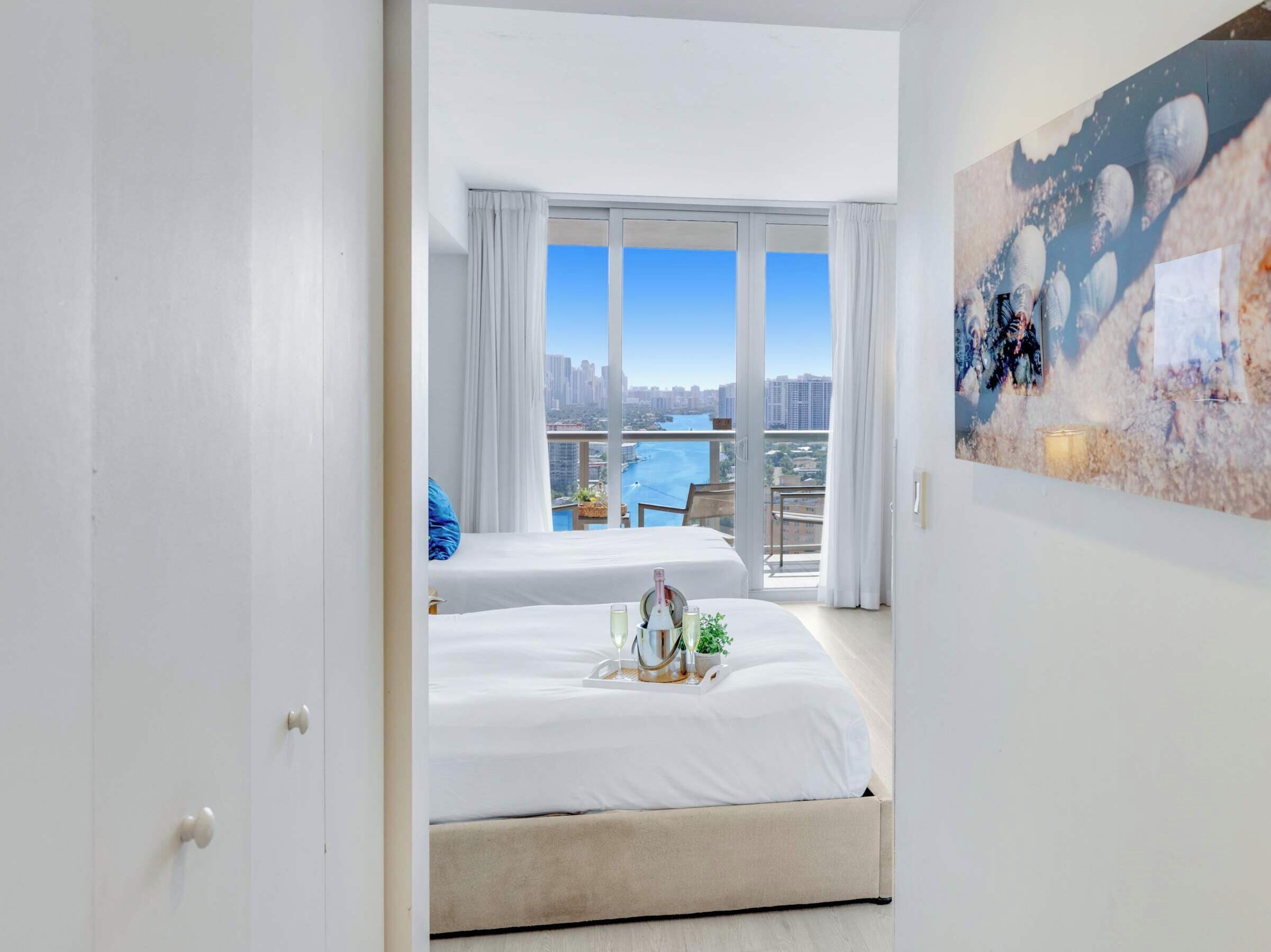 A hotel room with two beds, a balcony with a city view, and a painting on the wall.