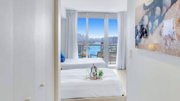 A hotel room with two beds, a balcony with a city view, and a painting on the wall.