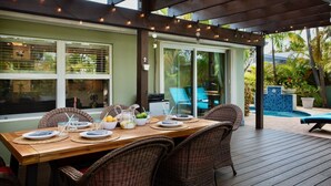 Een houten terras met een eettafel, omringd door rieten stoelen.