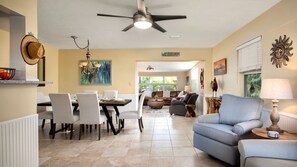 A spacious living area with a dining table, chairs, a sofa, and a ceiling fan.