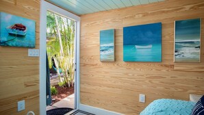 Een kamer met houten paneelwanden, een deur die uitkomt op een balkon met planten en drie ingelijste schilderijen van zeegezichten.