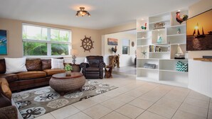 Een woonkamer met een bruine leren bank, een ronde rieten salontafel en een witte boekenkast vol decoratieve objecten.