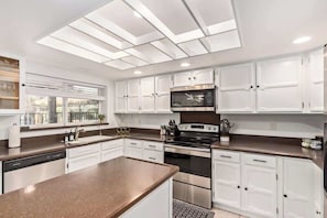 A modern kitchen with white cabinetry, a central island, a built-in oven, and a microwave. - Tiki Paradise w/Htd. Pool, Putt Grn. & Tiki Bar (Phoenix)