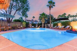 A swimming pool with lounge chairs and umbrellas, surrounded by palm trees and a wooden fence. - Tiki Paradise w/Htd. Pool, Putt Grn. & Tiki Bar (Phoenix)