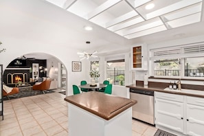 A modern kitchen with a central island, white cabinetry, and a dining area with green chairs. - Tiki Paradise w/Htd. Pool, Putt Grn. & Tiki Bar (Phoenix)