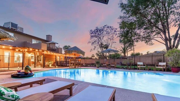 Une piscine avec des chaises longues, une structure à toit de chaume et une clôture en bois.