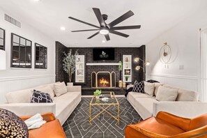 Ein modernes Wohnzimmer mit Kamin, zwei Sofas, einem Couchtisch und einem Deckenventilator.