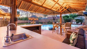 Un espace aménagé au bord de la piscine, doté d’un toit de chaume, d’un bar et de sièges.