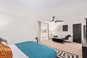A hotel room with a bed, a sofa, a desk, a ceiling fan, and a door. - Tiki Paradise |Heated Pool | Putt Grn. & Tiki Bar (Phoenix)