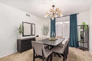A dining area with a table, chairs, a chandelier, a plant, and a bookshelf.