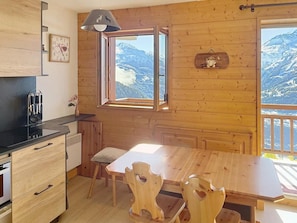 Interior de uma cabana de madeira com cozinha, mesa de jantar e cadeiras.