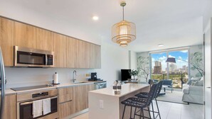 A modern kitchen with a built-in microwave, oven, and coffee maker. There is a bar area with stools and a view of the city through large windows. - One Bedroom Condo King Bed With City Views (Miami)