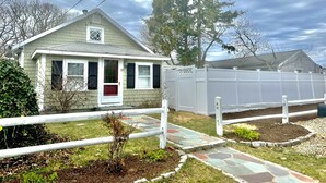 A single-story house with a porch, a white fence, and a small garden area with stepping stones. - Swan River Cottage - Near Beach, Water View, Kayak, (Dennis)