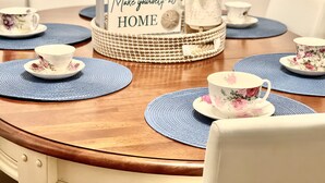A dining table with floral-patterned cups and saucers, blue placemats, and a decorative basket with a sign. - Swan River Cottage - Near Beach, Water View, Kayak, (Dennis)