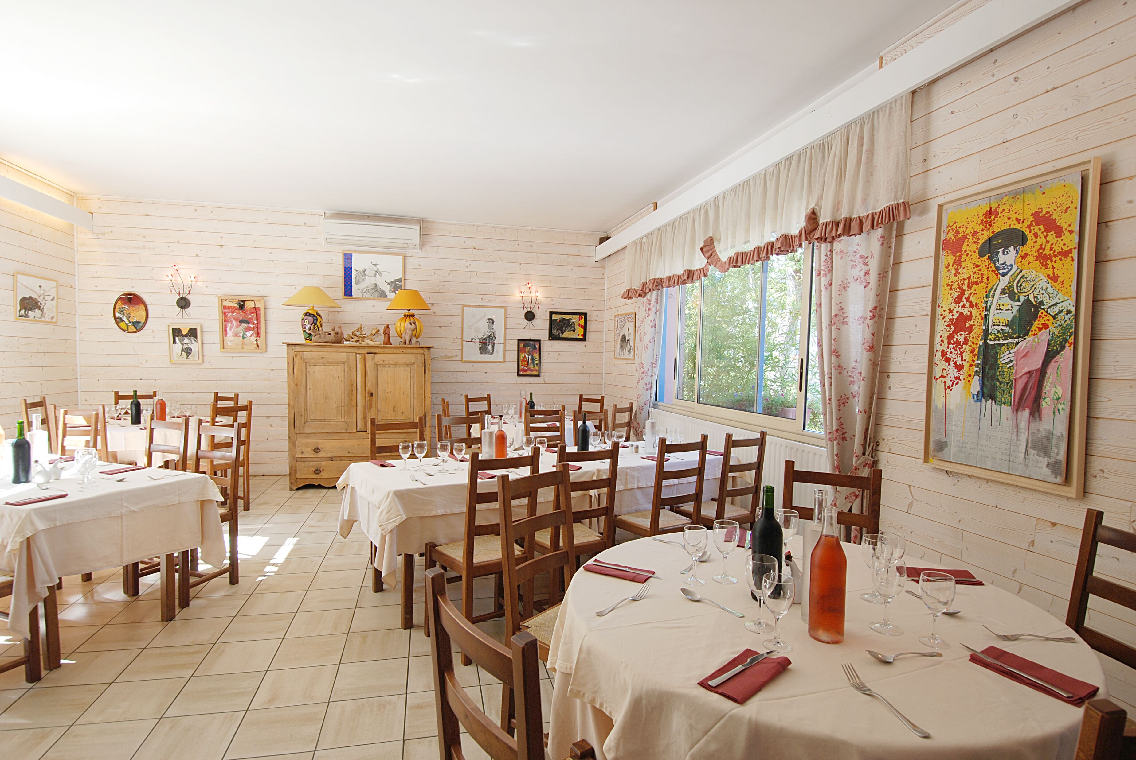 Zona de dinar amb diverses taules i cadires, parets de fusta i diferents quadres emmarcades.