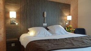 A hotel room with a large bed, two bedside lamps, a nightstand, and a wall-mounted telephone. - Hotel Restaurant des Thermes (Castera-Verduzan)