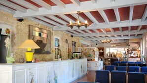 A lobby with a reception desk, blue chairs, and a stone wall with artwork. - Hotel Restaurant des Thermes (Castera-Verduzan)