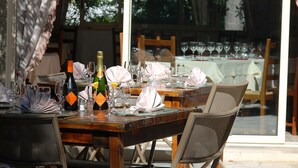 An outdoor dining area with wooden tables and chairs, set for a meal with wine glasses and a bottle of champagne. - Hotel Restaurant des Thermes (Castera-Verduzan)