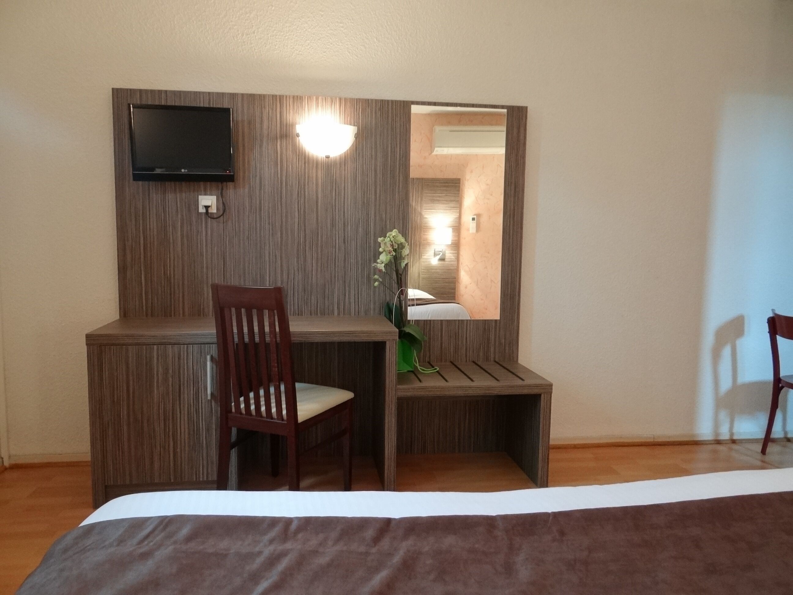 Een hotelkamer met een bed, een bureau, een stoel, een televisie en een spiegel.