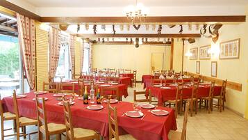 A dining area with multiple tables set for meals, wooden chairs, and a chandelier.