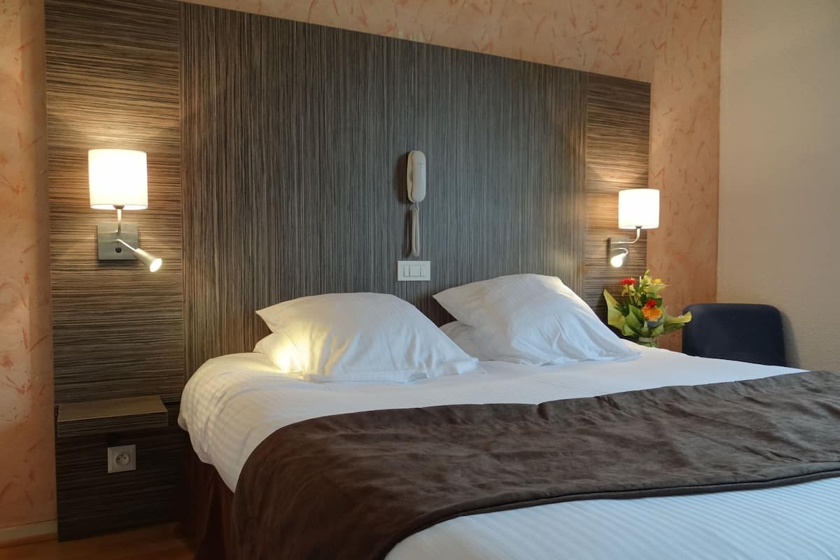 A hotel room with a large bed, two bedside lamps, a nightstand, and a wall-mounted telephone.