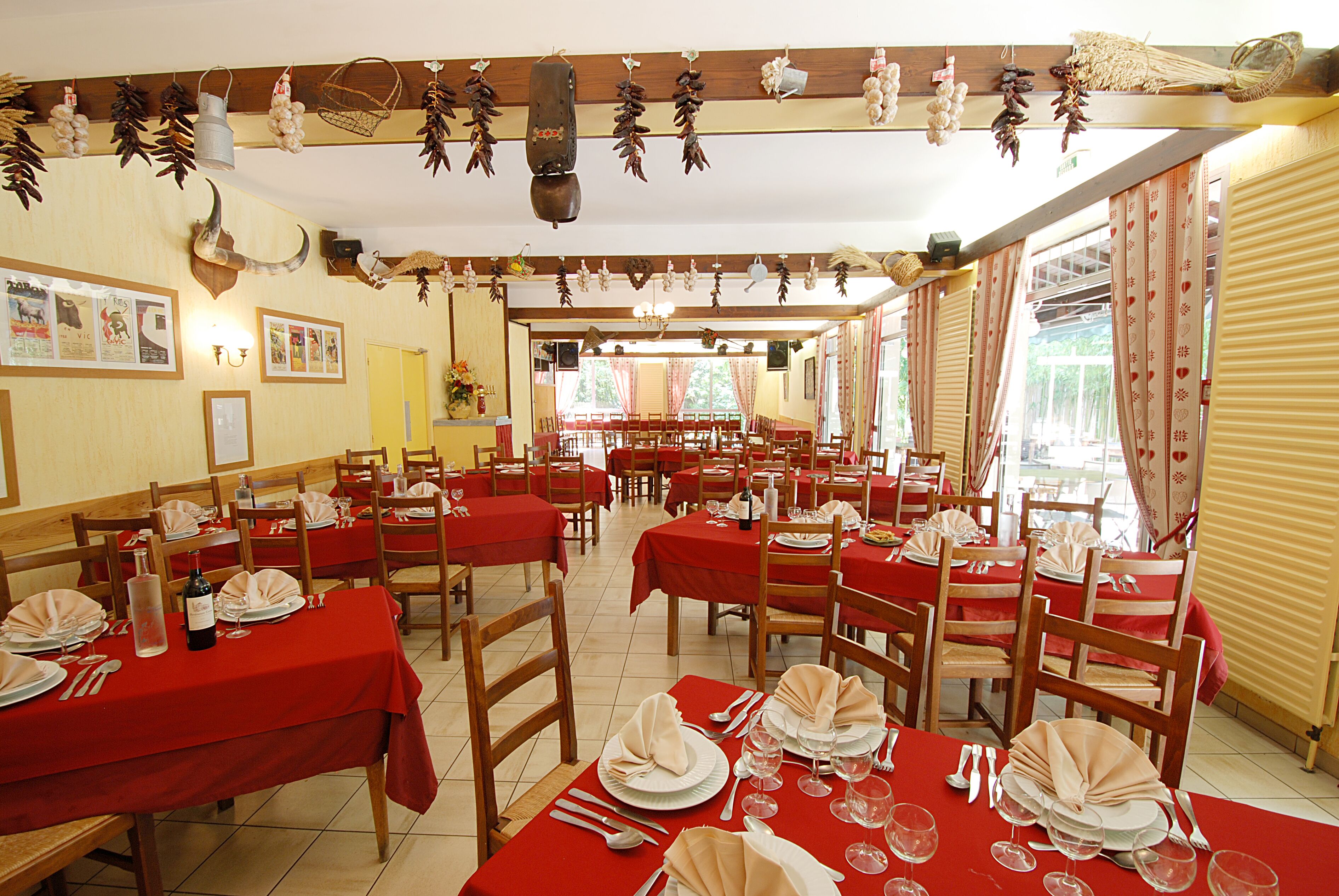 A restaurant with multiple tables set for dining, featuring red tablecloths and wooden chairs.