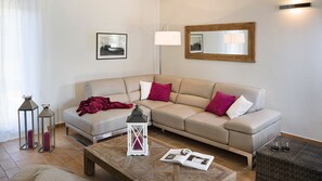 Un salon avec un canapé beige, deux tables d’appoint, une table basse et un miroir au mur.