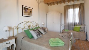A bedroom with a bed, a nightstand, a lamp, a wardrobe, and a window with curtains. - Villa Elettra 12+2 by Marche Holiday Villas (San Costanzo)