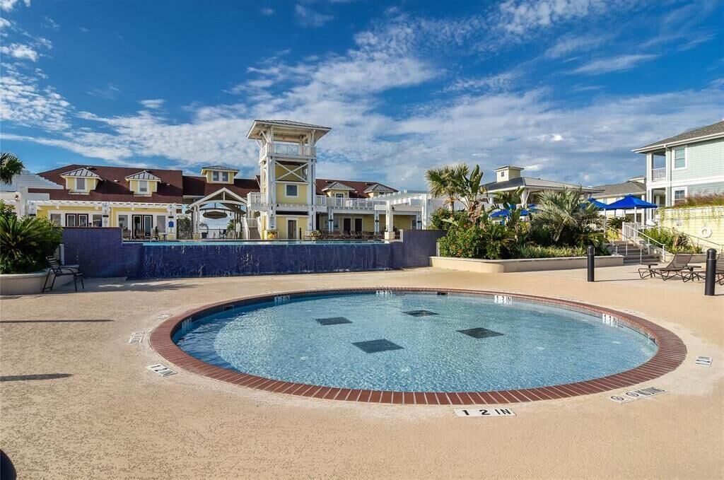 A swimming pool with a brick border and a 12-inch depth marker, surrounded by a landscaped area with palm trees and lounge chairs.